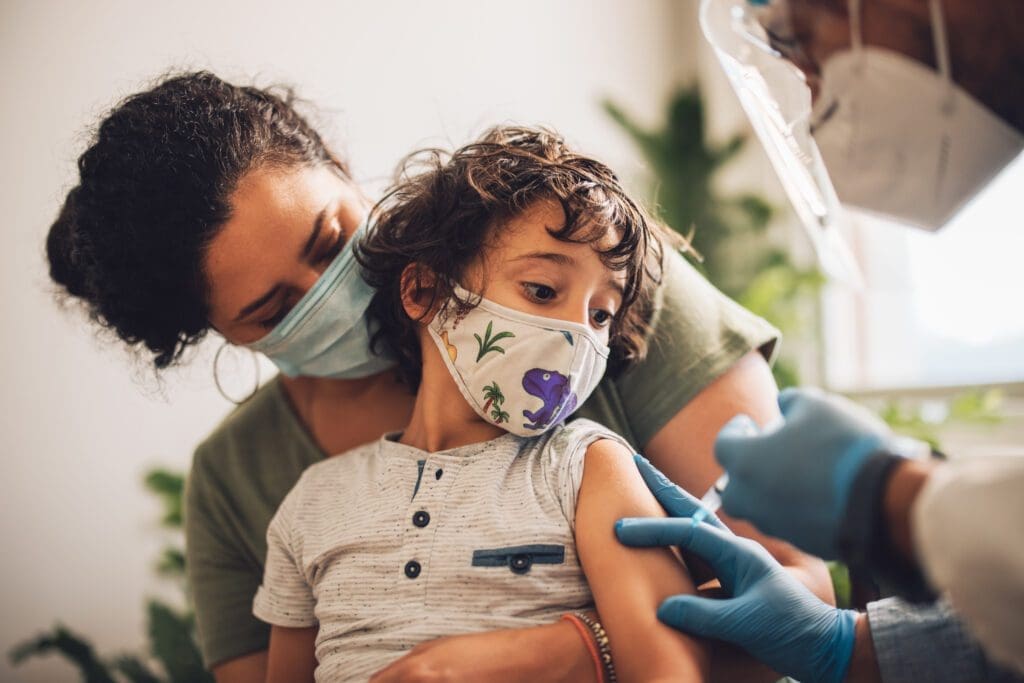 image of child wearing face mask receiving vaccine with parent.